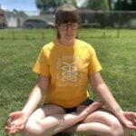 Kristi wearing a yellow shirt sitting in a meditation pose